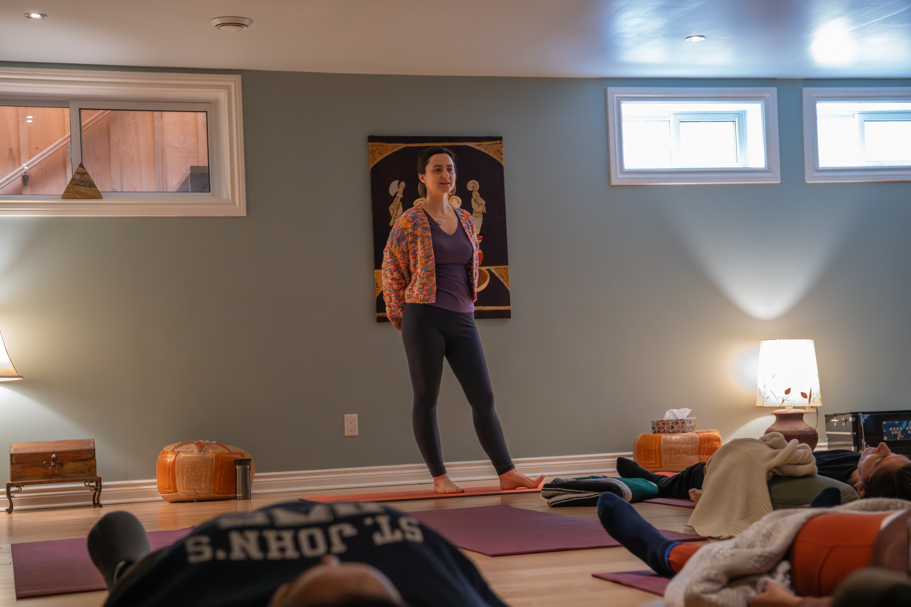 Zofia standing in her home yoga studio with students resting on mats